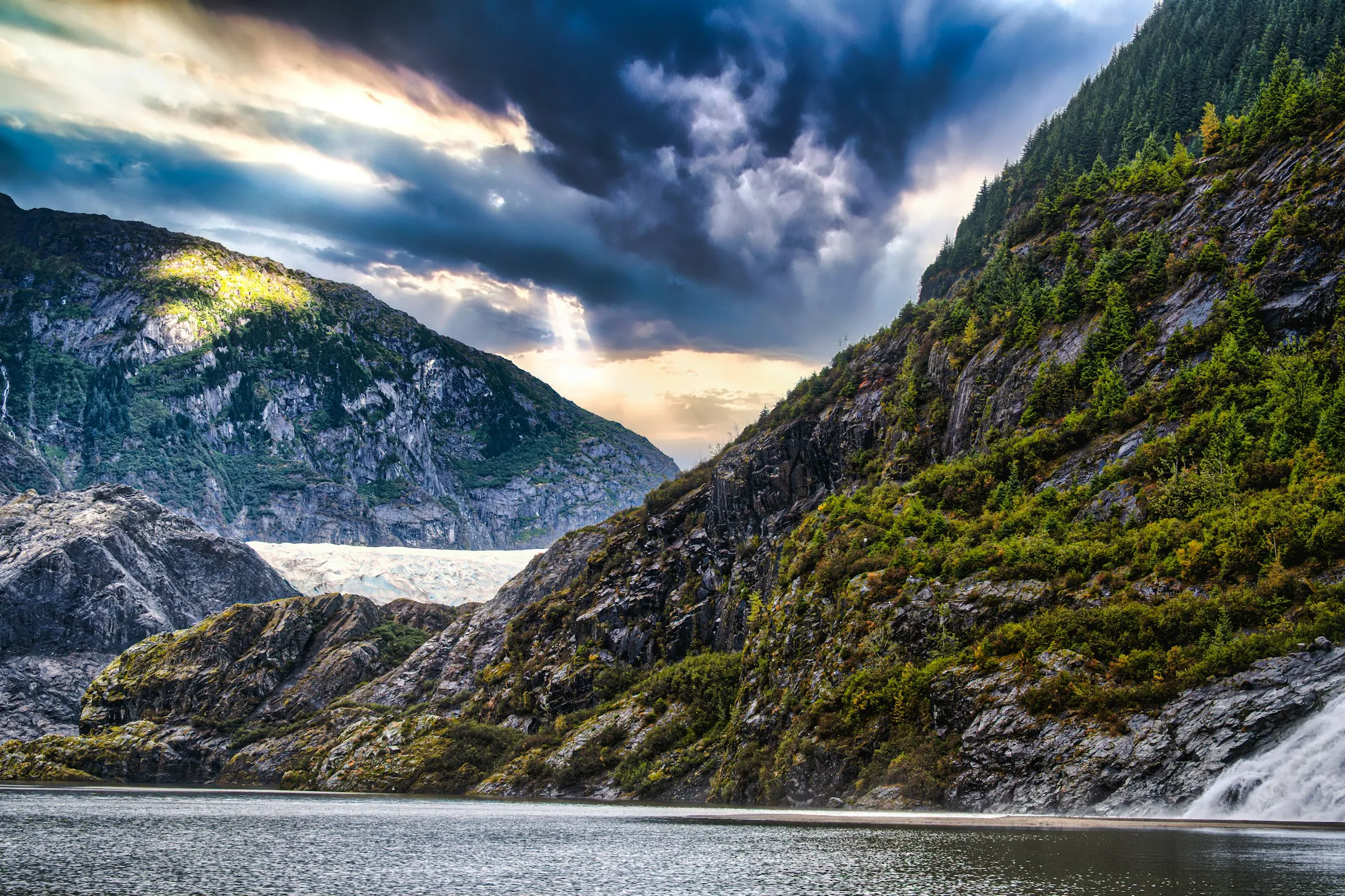 Rugged Alaskan mountains and waterfalls under a dramatic sky