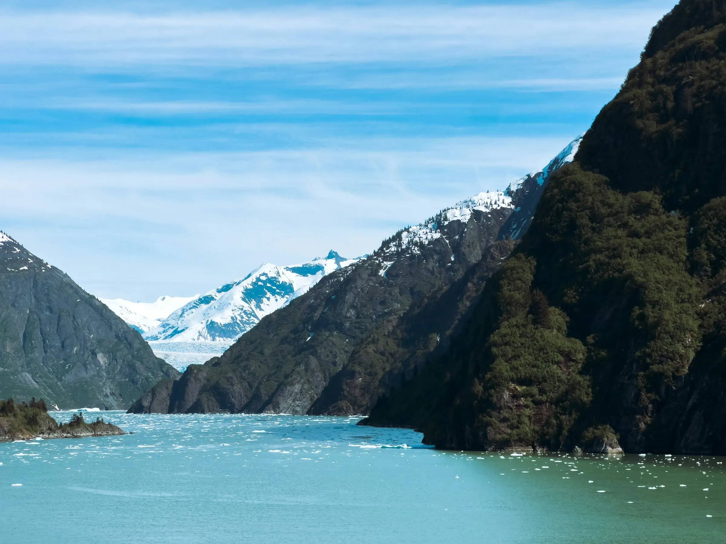 A narrow turquoise fjord between steep green cliffs in Alaska