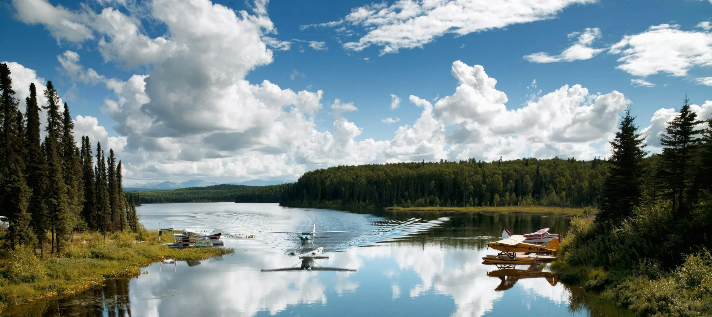 Floatplanes resting on a mirror-calm Alaskan lake under big clouds