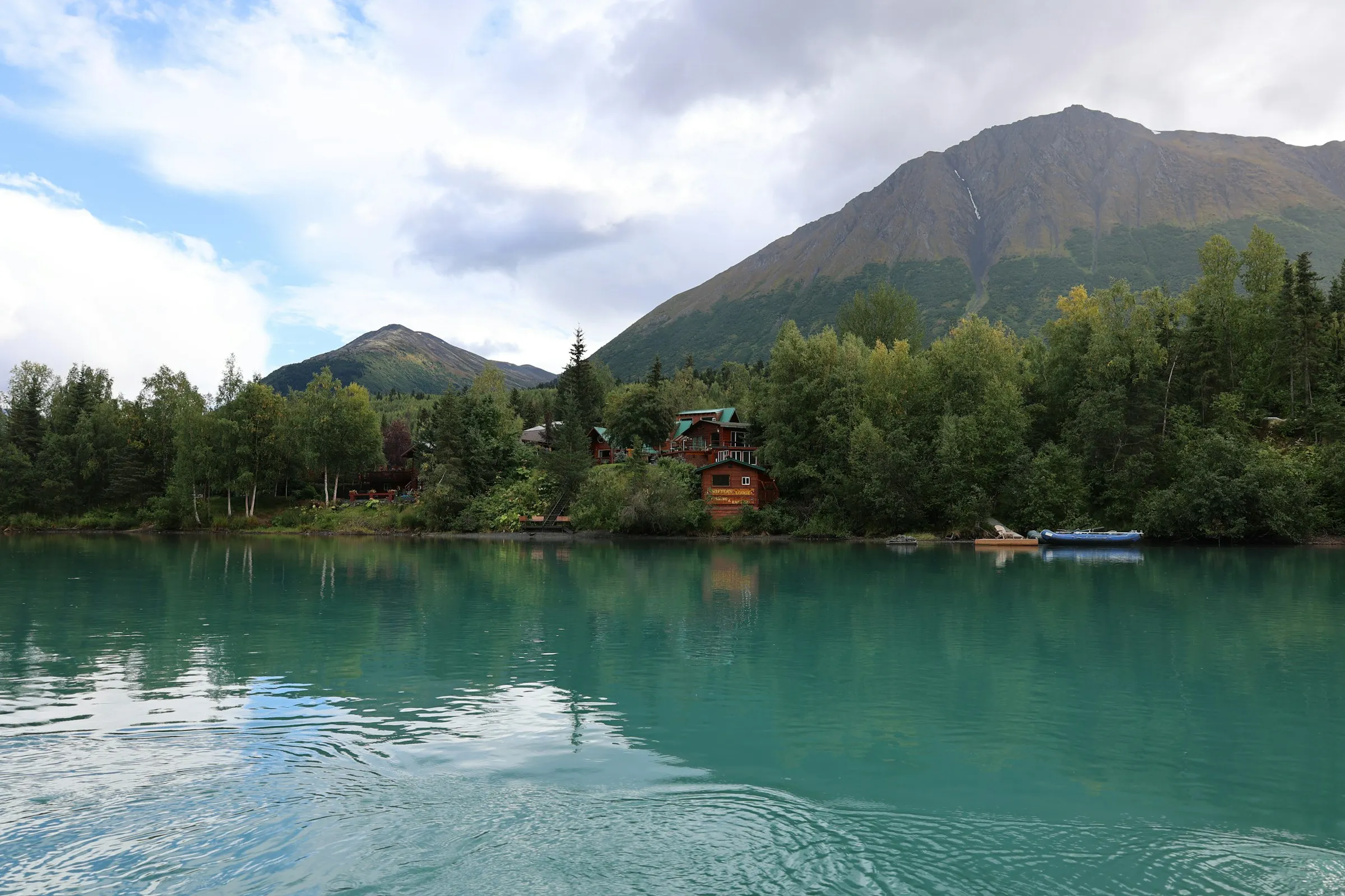 A lakeside lodge below green Alaskan mountains