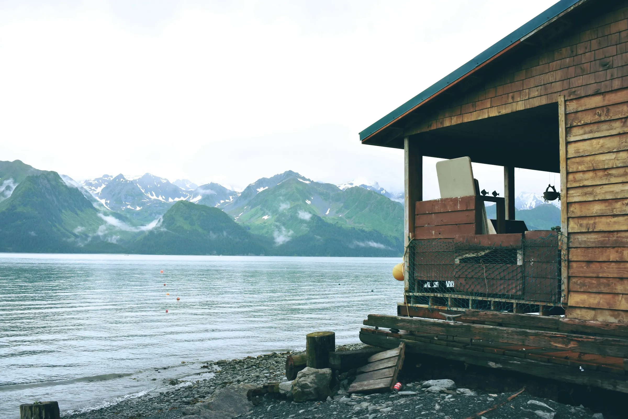 A cedar fishing cabin on the shore with mountains across the water