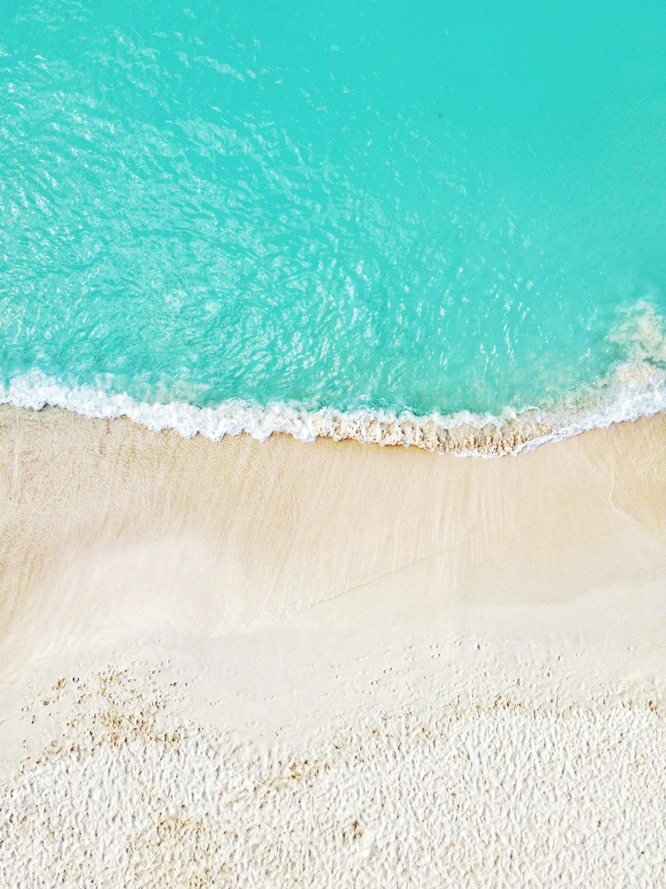 Aerial view of a wave rolling onto pale sand