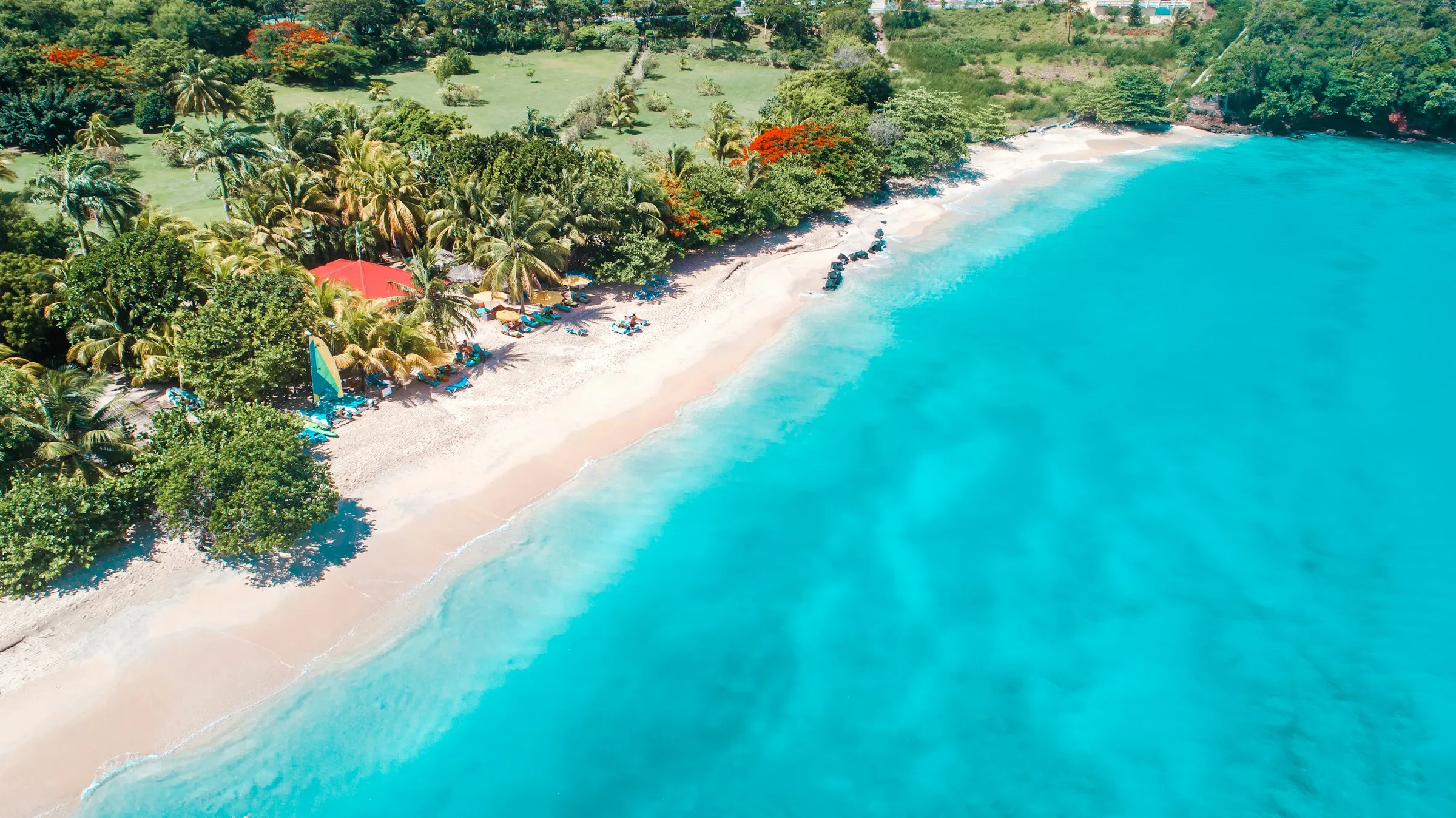 Aerial view of a white-sand beach, turquoise water and a strip of palms