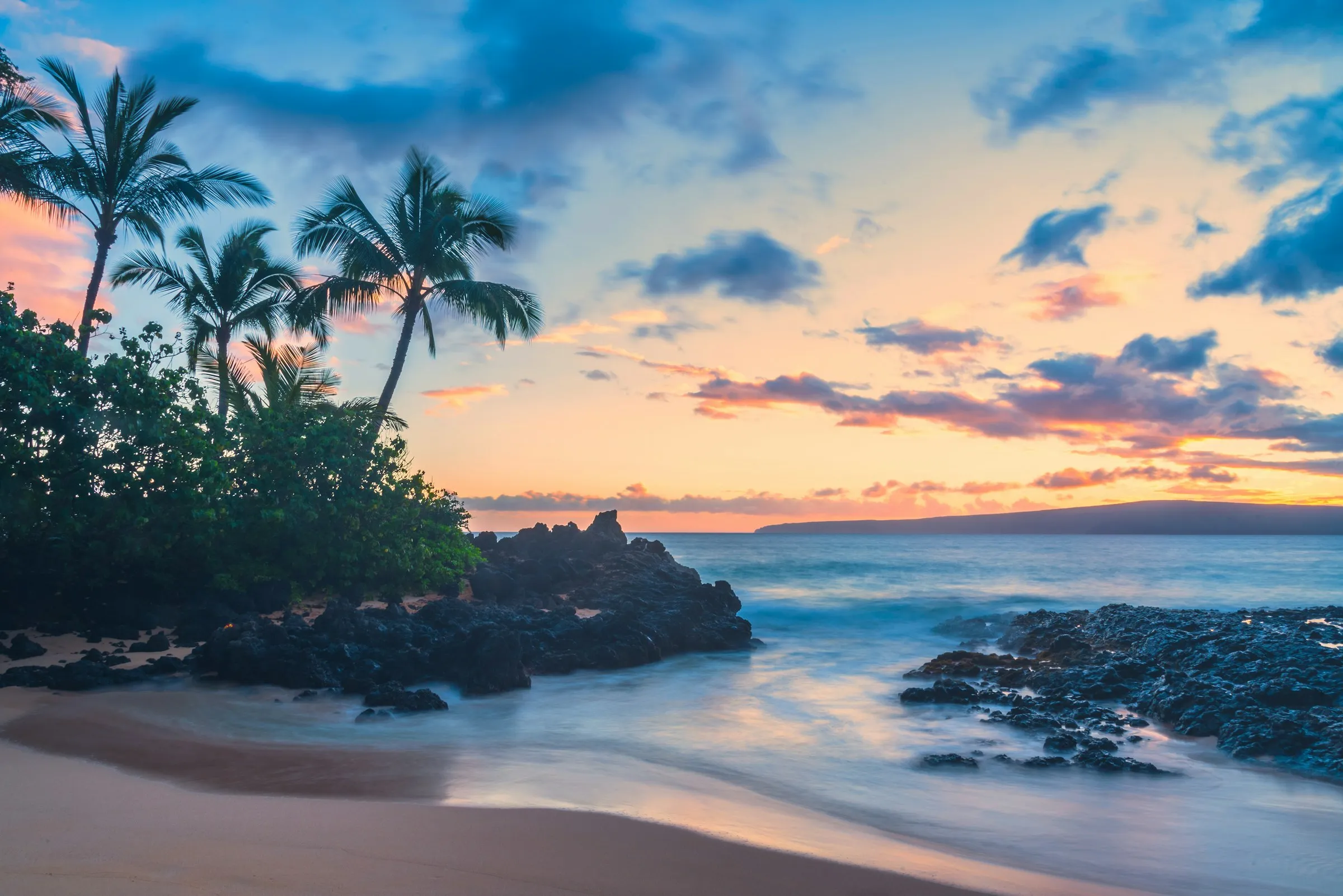 A Maui cove at sunset with palms and lava rock