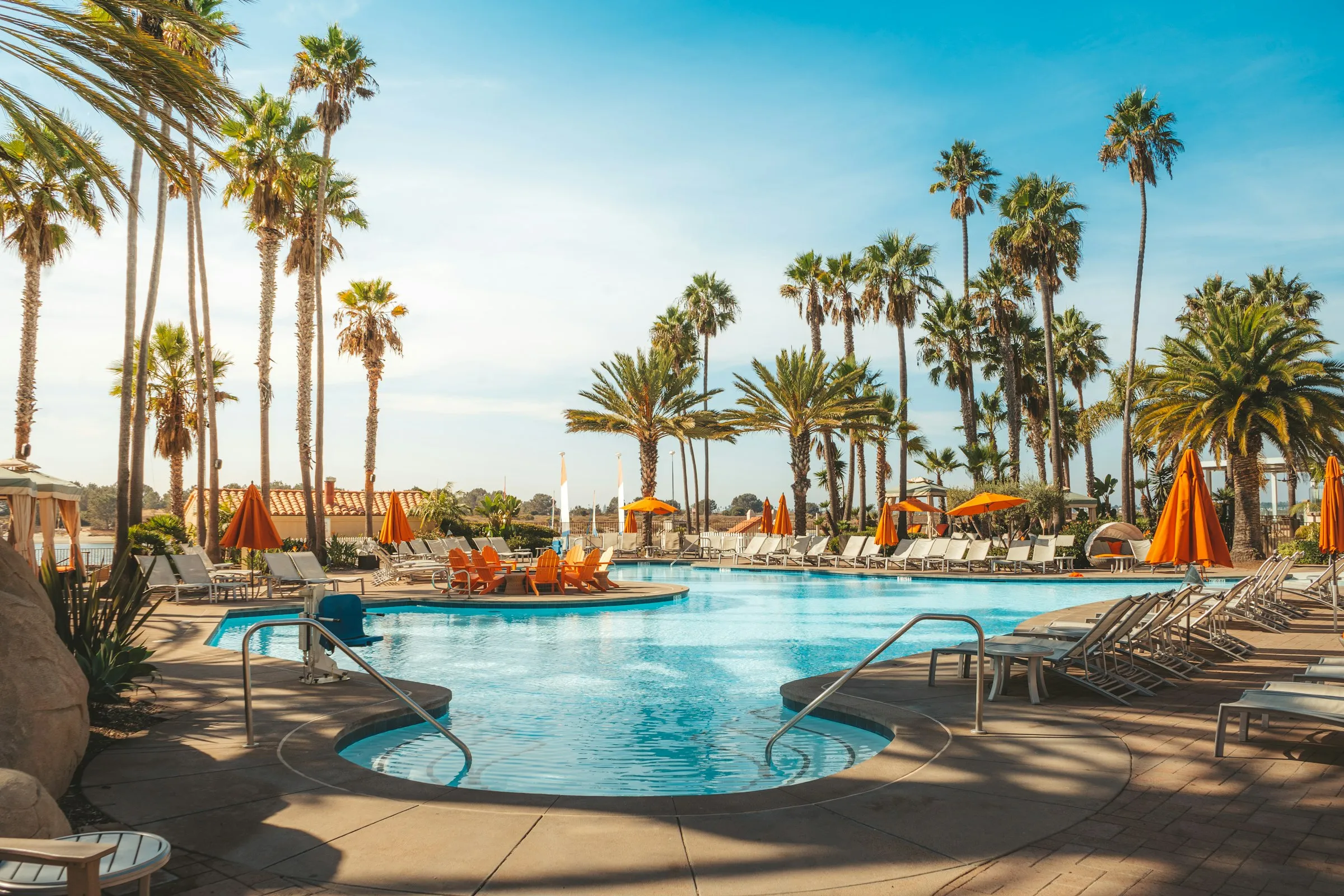 A resort pool ringed with palms and orange umbrellas