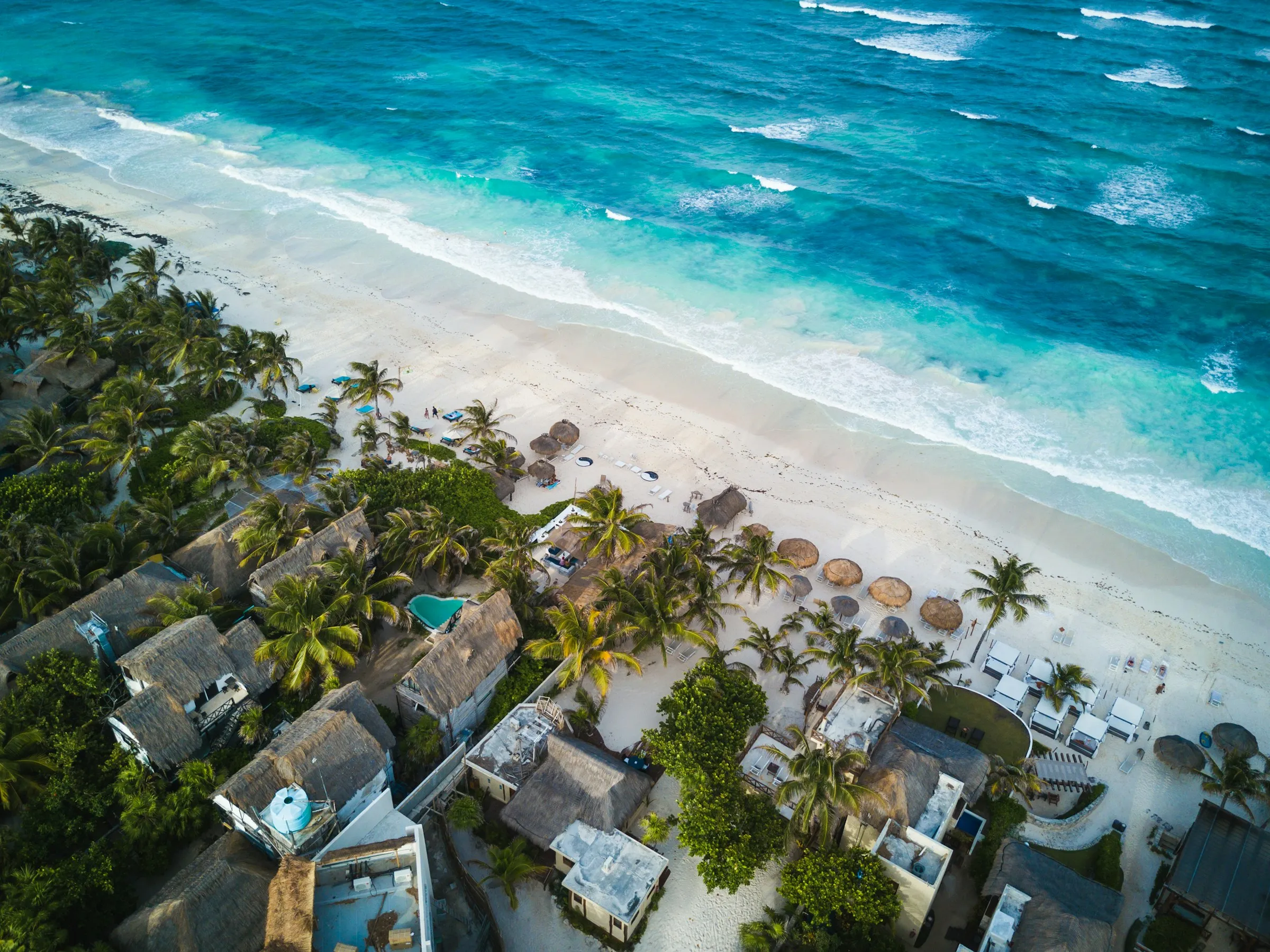 Aerial view of a Riviera Maya resort beach with palapas and palms
