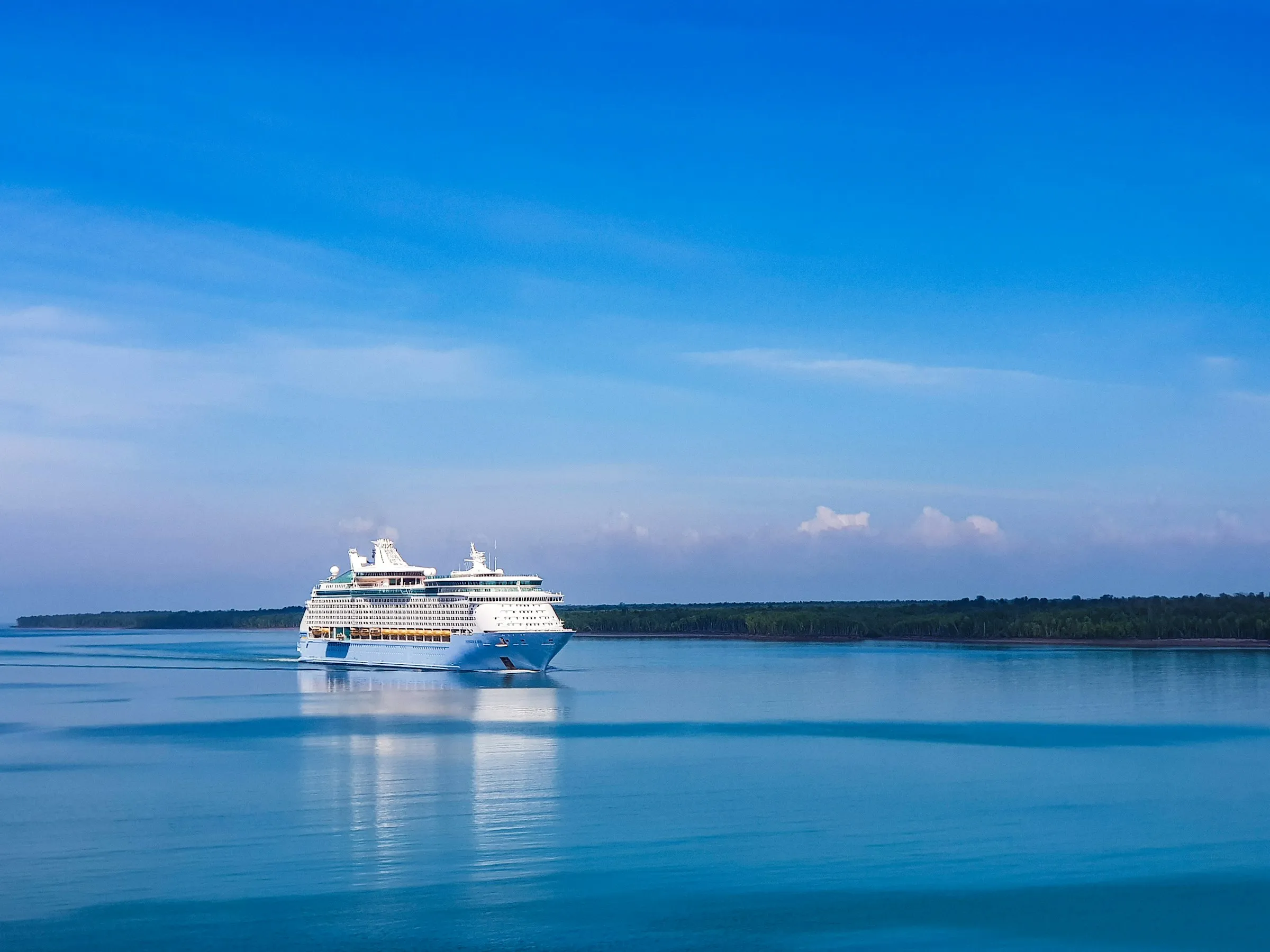A cruise ship on calm blue water near a green coast