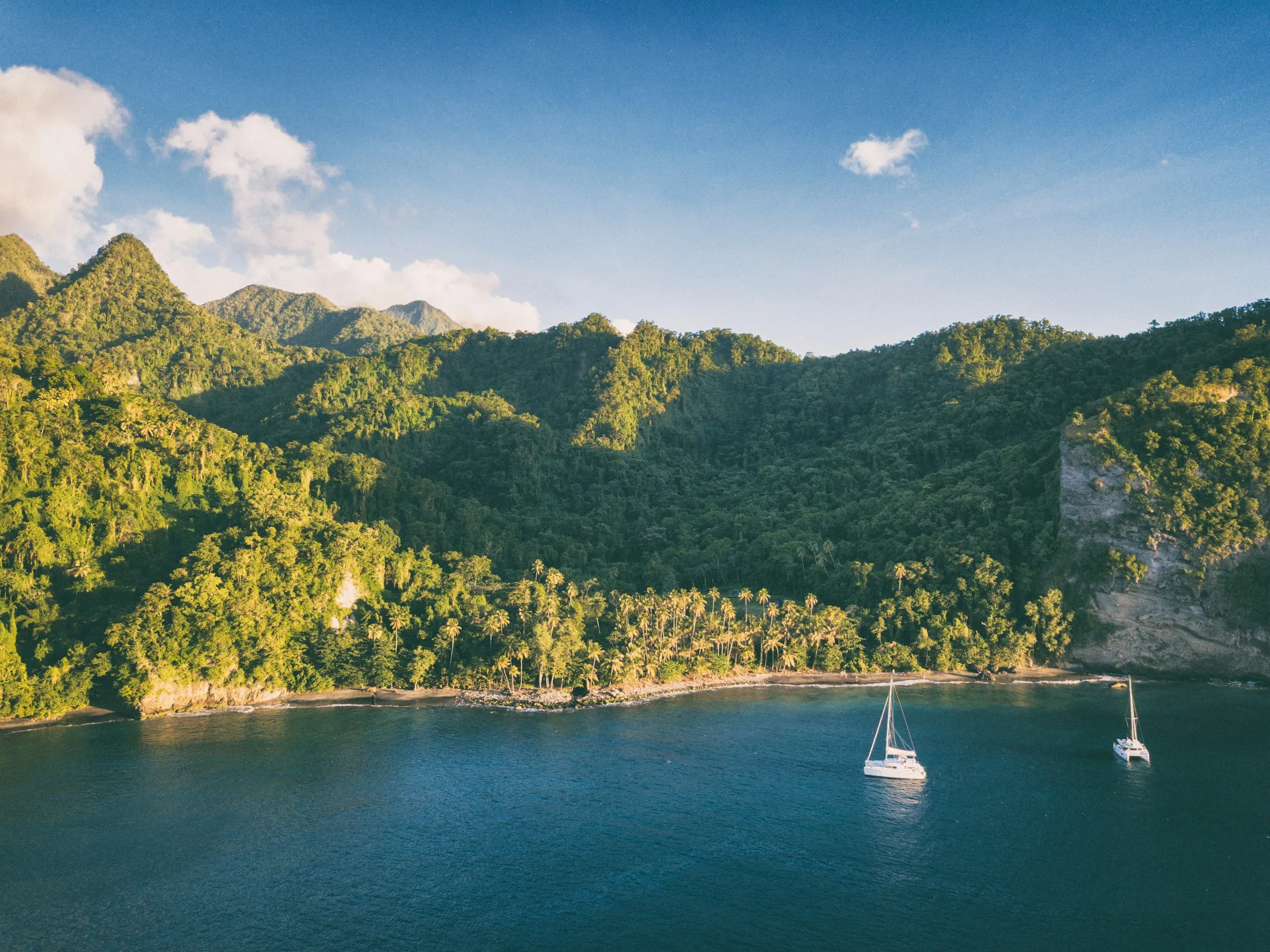 A sailboat anchored beneath green Caribbean hills