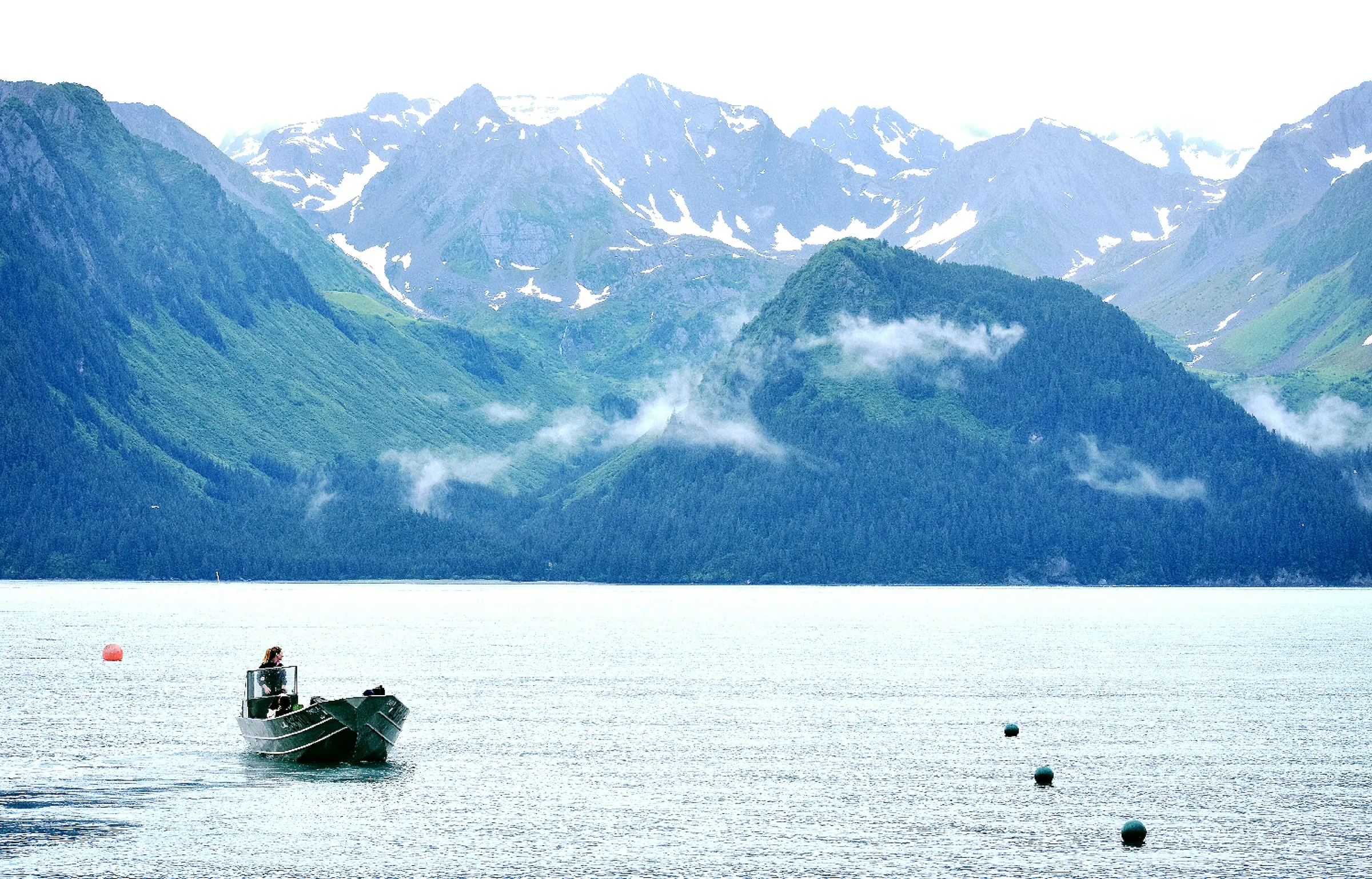 A small fishing boat on glassy water beneath snow-streaked Alaskan mountains