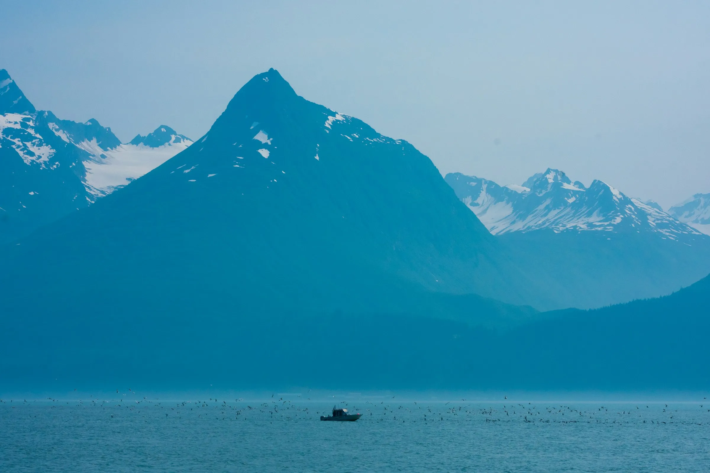 A lone boat crossing a deep blue fjord under towering blue mountains