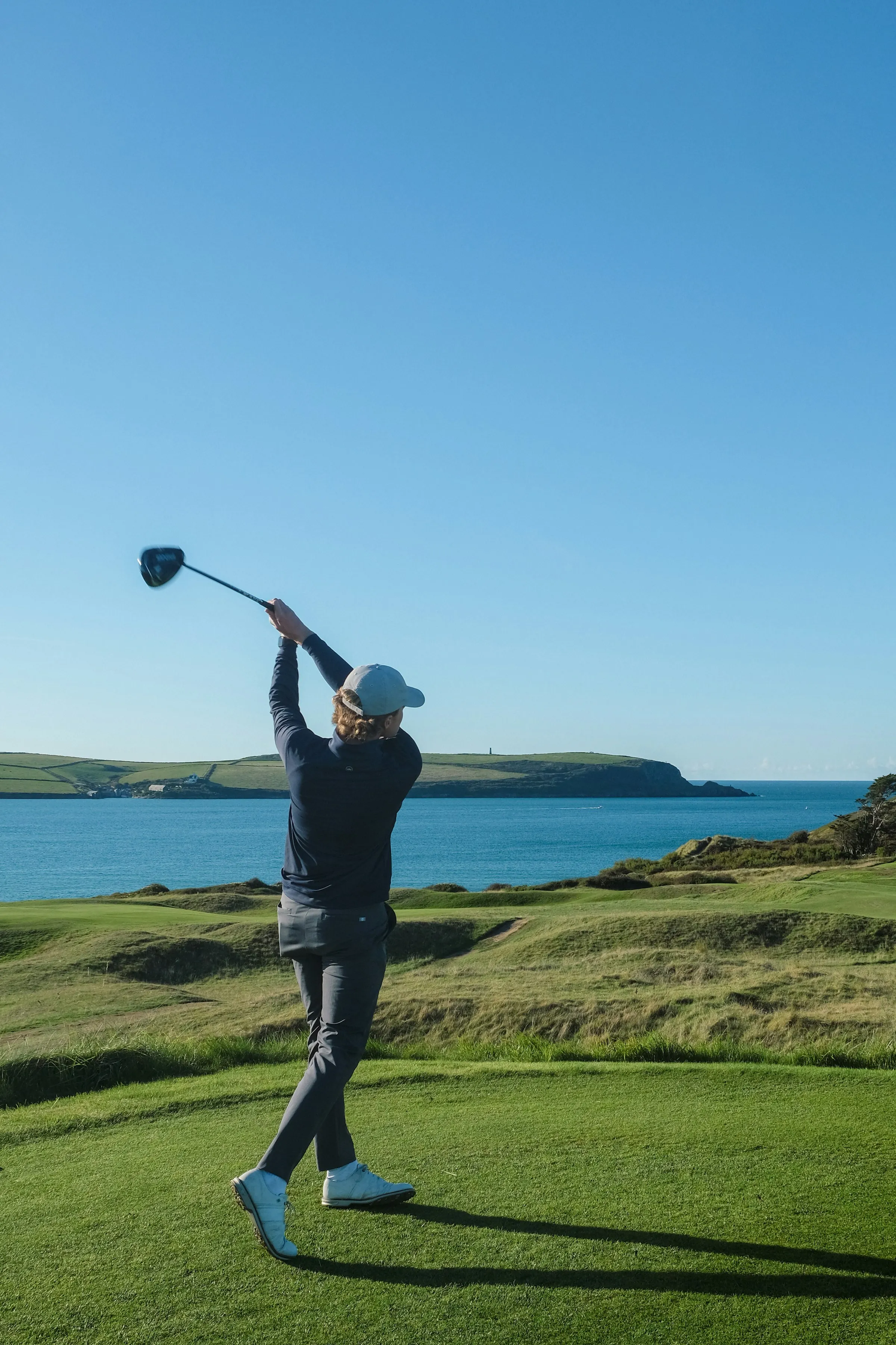 A golfer finishing a drive with the ocean behind