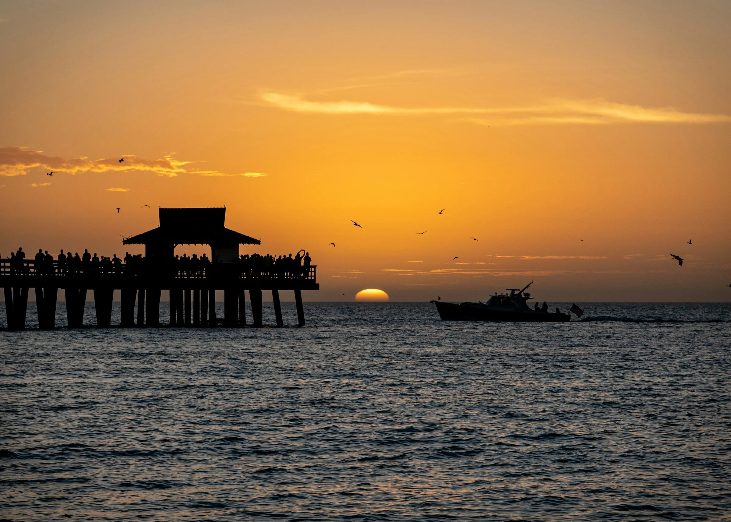 The Naples Pier at sunset with a boat passing